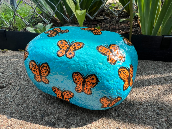 A painted rock with a blue background and monarch butterflies painted on it.